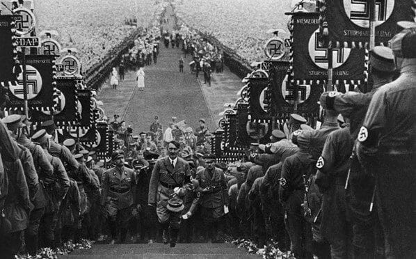 Adolf Hitler, German dictator, ascending the steps at Buckeberg flanked by banner-carrying storm troopers who display the Nazi swastika.
